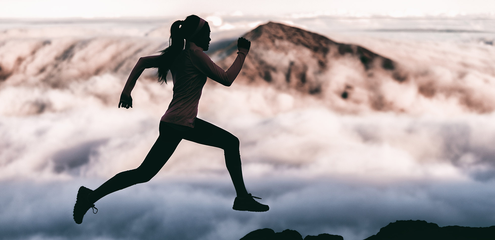 woman running atop a mountain with clouds in the background