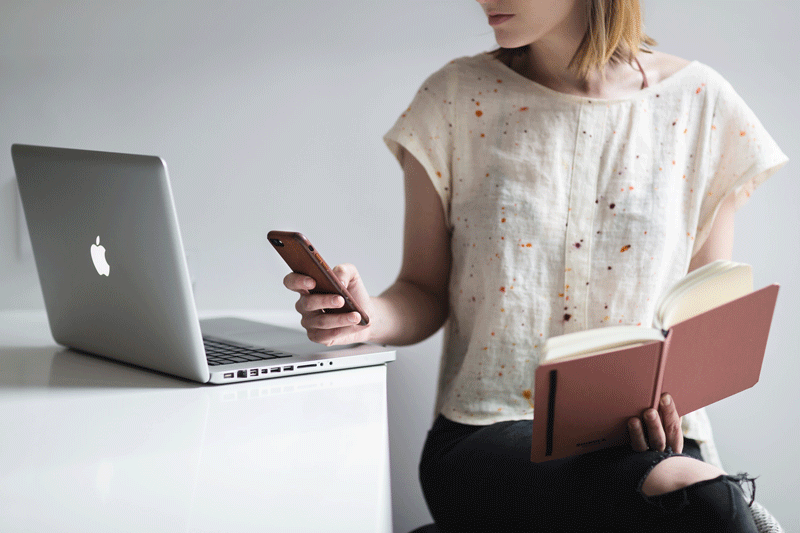 Burst.com photo of woman trying to read a book, type on her computer, and look at her phone at the same time